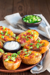 Baked loaded potato skins with cheddar cheese and bacon, garnished with scallions and sour cream vertical