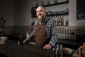 Portrait of a handsome young barista in apron sitting at the bar of the modern cafe
