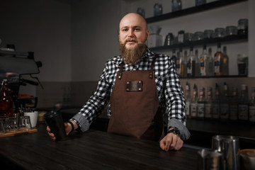 Portrait of a handsome young barista in apron sitting at the bar of the modern cafe