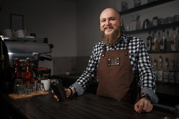 Portrait of a handsome young barista in apron sitting at the bar of the modern cafe