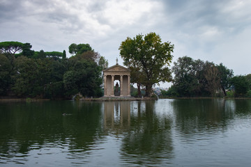 Fototapeta na wymiar A pond and ancient pavillion with statues in the park of Villa Borghese shot on a rainy October day