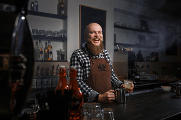 Portrait of a handsome young barista in apron sitting at the bar of the modern cafe