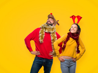 Couple dressed up for the christmas holidays posing with arms at hip and laughing on yellow background