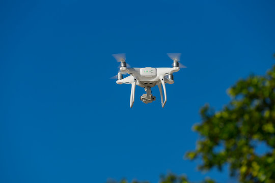 Drone in flight, green trees in the background, selective focus on the drone.