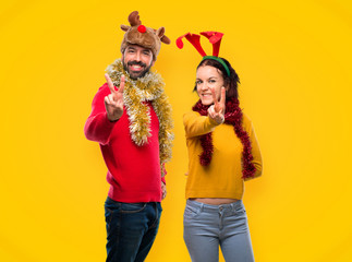 Couple dressed up for the christmas holidays smiling and showing victory sign on yellow background
