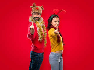 Couple dressed up for the christmas holidays showing and lifting a finger in sign of the best on isolated red background