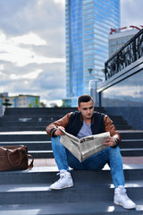 Fototapeta na wymiar portrait of young guy in leather jacket reading newspaper in the cit