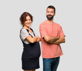 Couple with pregnant woman keeping the arms crossed in lateral position while smiling on isolated grey background