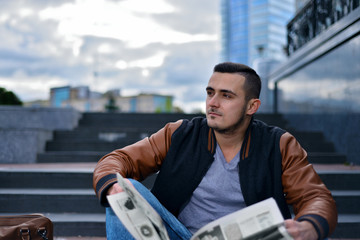 portrait of young guy in  leather jacket reading newspaper in the city