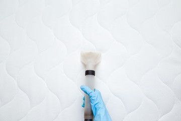 Employee hand in blue protective glove cleaning new modern white mattress with professionally...