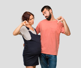 Couple with pregnant woman showing thumb down sign with negative expression on isolated grey background