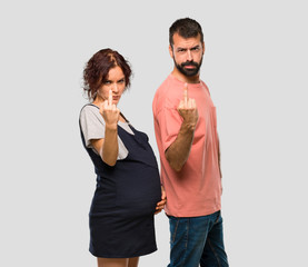 Couple with pregnant woman making horn gesture. Negative expression on isolated grey background