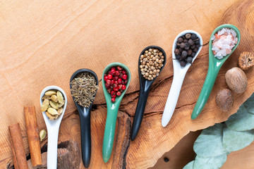 Exotic herbal Food concept Mix of the organic Spices cinnamon stick, cardamom pods, cumin, black pepper, pink peppercorn, nutgeg and coriander seeds in white ceramic spoon on a wood background - Powered by Adobe