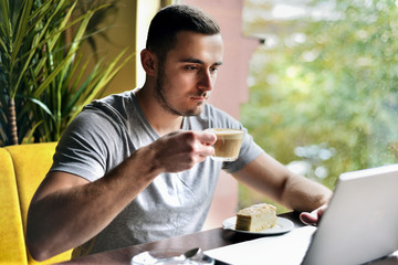 young guy is freelancer in cafe working behind a laptop. man drinking coffee