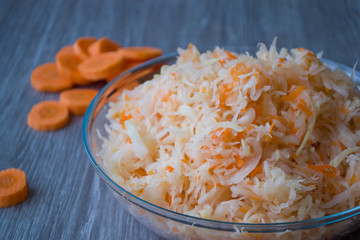 Orange carrot pieces and Salted chopped cabbage with carrots in a Cup on a wooden background.