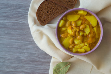 Photo bean soup in a plate and pieces of bread on a light napkin and a wooden table.