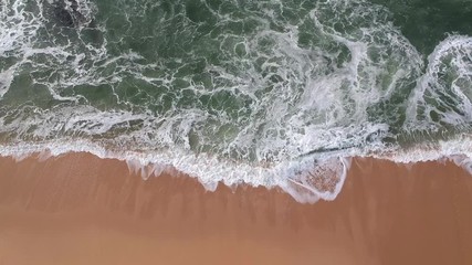 High overhead aerial shot of waves crashing on sandy beach in Portugal