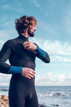Young man putting on wetsuit near sea