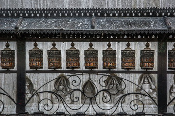Close up view of metal fence with dozen buddhist prayer wheel. Kathmandu, Nepal.