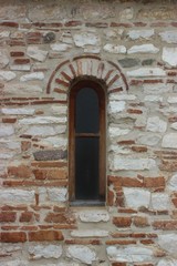 Fototapeta na wymiar Closed window in a wall made of stones and ceramic bricks at a very old byzantine orthodox church