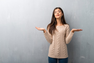 Teenager girl with sweater on a vintage wall having doubts while raising hands and shoulders