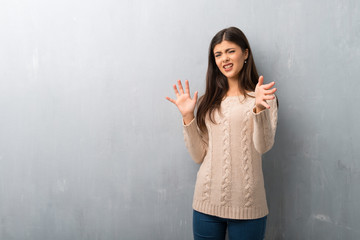 Teenager girl with sweater on a vintage wall is a little bit nervous and scared stretching hands to the front