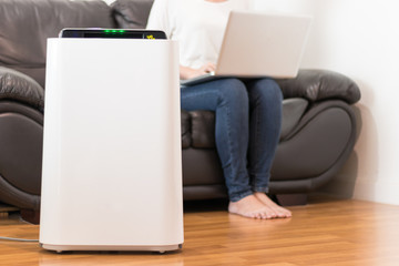 Air purifier in a living room, woman working with laptop with filter for clean room