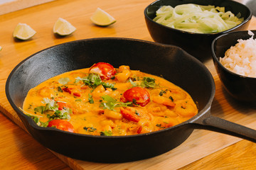 Shrimp with curry on black pan. Wooden background with lime, onion and rise
