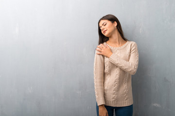 Teenager girl with sweater on a vintage wall suffering from pain in shoulder for having made an effort
