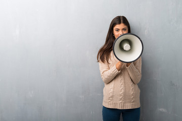 Teenager girl with sweater on a vintage wall shouting through a megaphone to announce something
