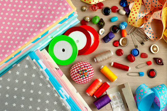 Cotton fabric and items for sewing. View from above. A pile of cotton fabric, decorative ribbons, spools of thread, buttons, needles for sewing clothes or bed linen.