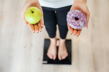 Diet. Woman Measuring Body Weight On Weighing Scale Holding Donut and apple. Sweets Are Unhealthy...