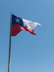 Flag of Chile flies in a strong wind against a bright blue sky with sun glare