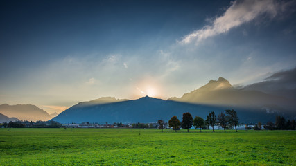 volume light beams of sunset sun behind peak of mountain chain in austria holiday