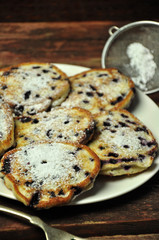 Pancakes with blueberries sprinkled with powdered sugar on a white plate on a wooden background