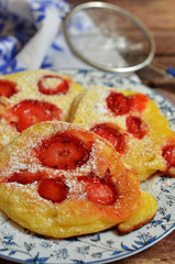 Pancakes with strawberries sprinkled with powdered sugar on a rustic plate on a wooden background