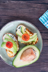 Toasts with avocado pieces, cherry tomatoes, scrambled eggs and soft cream cheese.