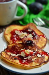 Pancakes with plum jam and almond flakes on a white plate