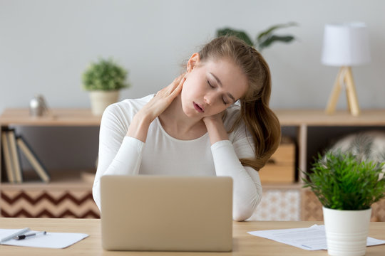 Exhausted Young Female Sit At Home Office Desk Massaging Neck Feeling Ache, Tired Girl Suffer From Back Pain Or Strain, Having Spasm Symptoms, Millennial Woman Feel Unwell From Sedentary Lifestyle