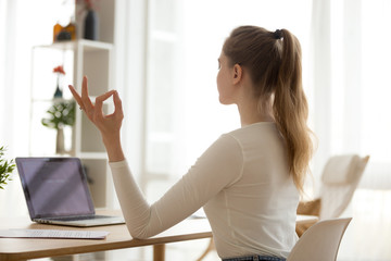 Calm female sit at work desk meditating with hands in mudra position, focused girl practice yoga at office table at home, controlling emotions and relieving stress, woman balance breathing fresh air