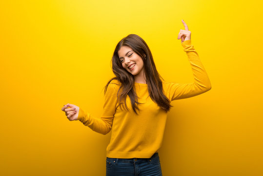 Teenager girl on vibrant yellow background enjoy dancing while listening to music at a party