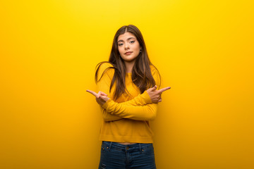 Teenager girl on vibrant yellow background pointing to the laterals having doubts