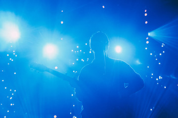 Rock band front man silhouette on a stage with guitar singing to microphone in colorful backlights 
