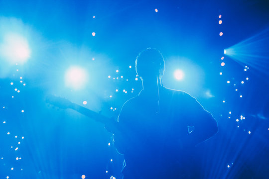 Rock band front man silhouette on a stage with guitar singing to microphone in colorful backlights 