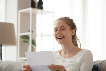 Excited girl sit on couch reading letter knowing good news, happy young female look through...