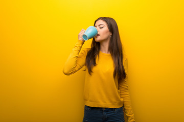 Teenager girl on vibrant yellow background holding a hot cup of coffee