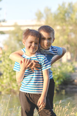 Two boys of three years in white T-shirts, jeans and caps are sitting on the grass and hugging. Two close friends, two cousins. Family relations between brothers