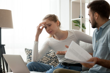 Millennial couple have fight over documents at home, man and woman sit on couch upset about bad...
