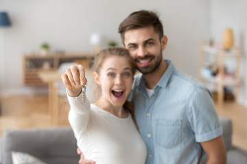 Portrait of happy millennial couple hug holding key to own apartment, young husband and wife excited to buy first home together, smiling married man and woman move in shared house. Ownership concept