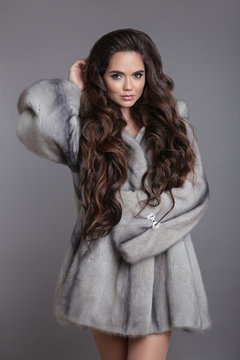 Elegant woman in mink fur coat isolated on gray studio background. Brunette Girl in Luxury Winter outerwear.